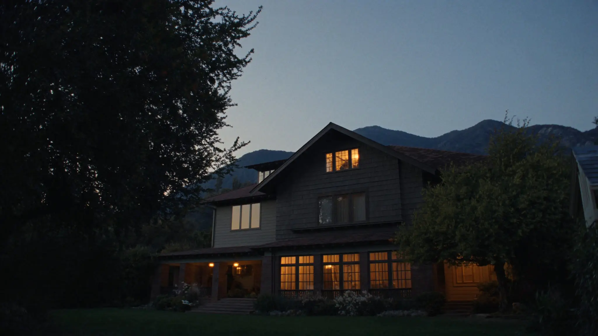 Three-story shingled home glowing at dusk in Altadena, the San Gabriel foothills rising behind