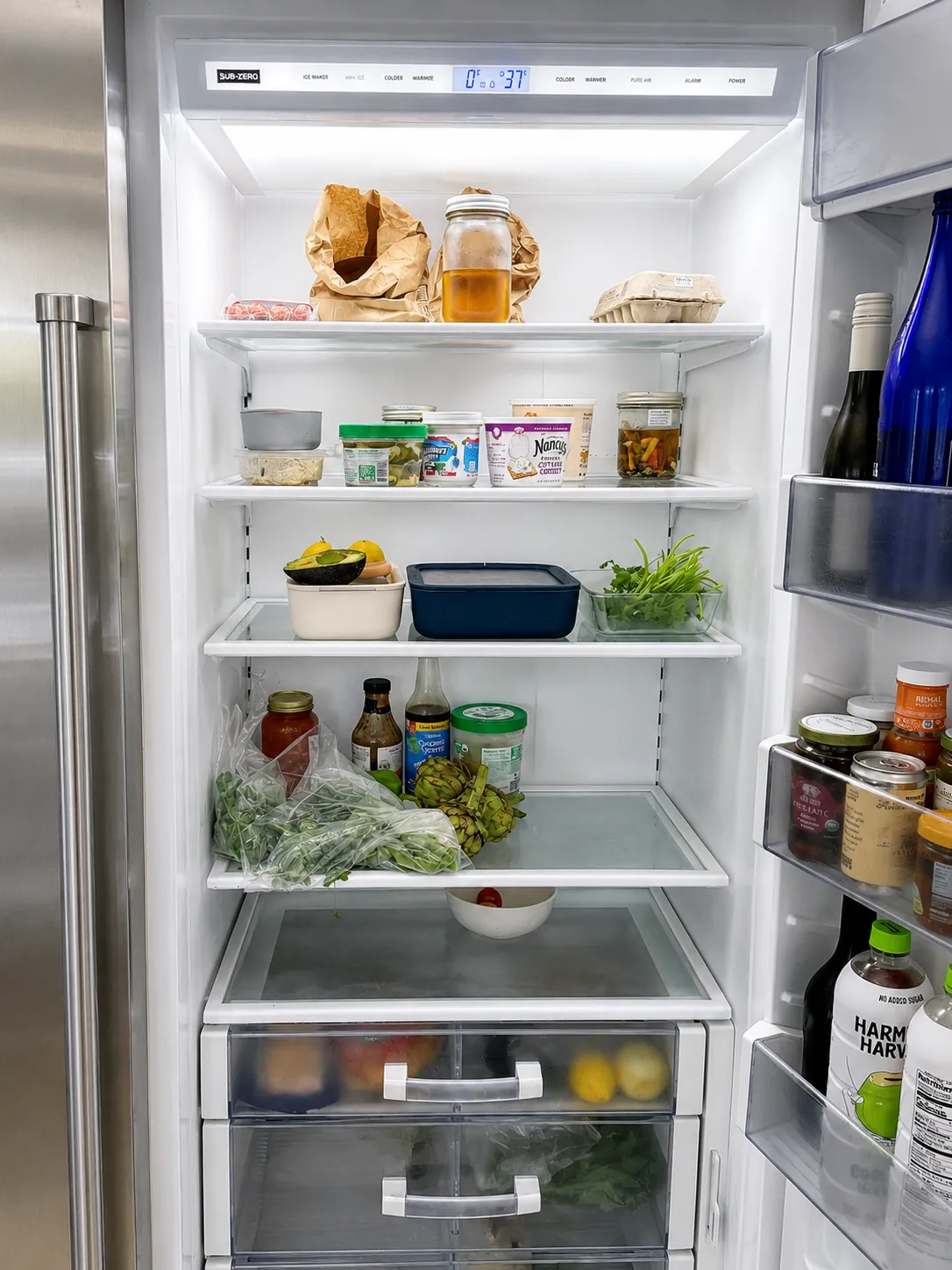 Inside an open Sub-Zero refrigerator column — stocked shelves under the temperature control panel