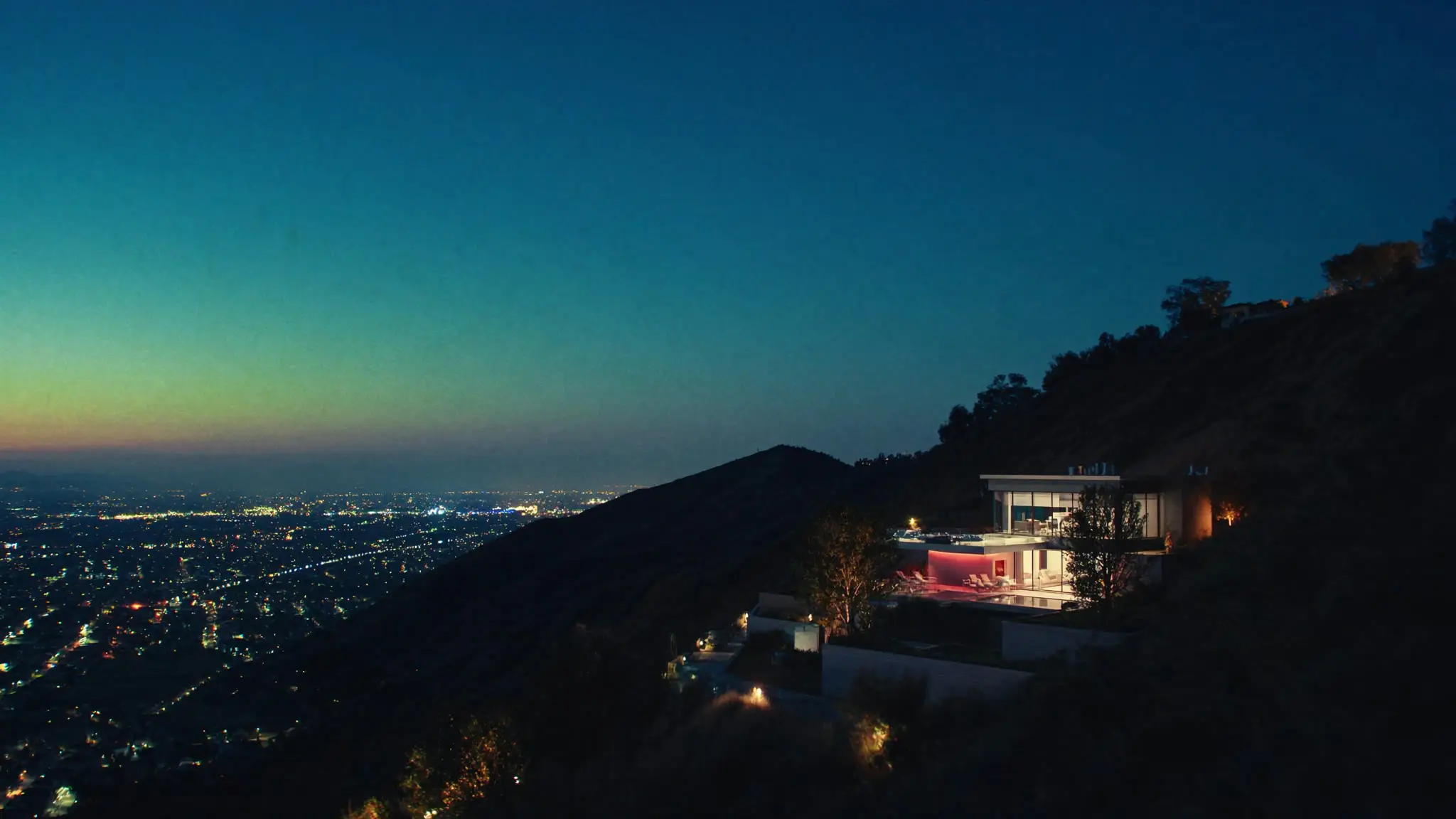 Modern glass house in the Hollywood Hills at dusk, city lights spreading below