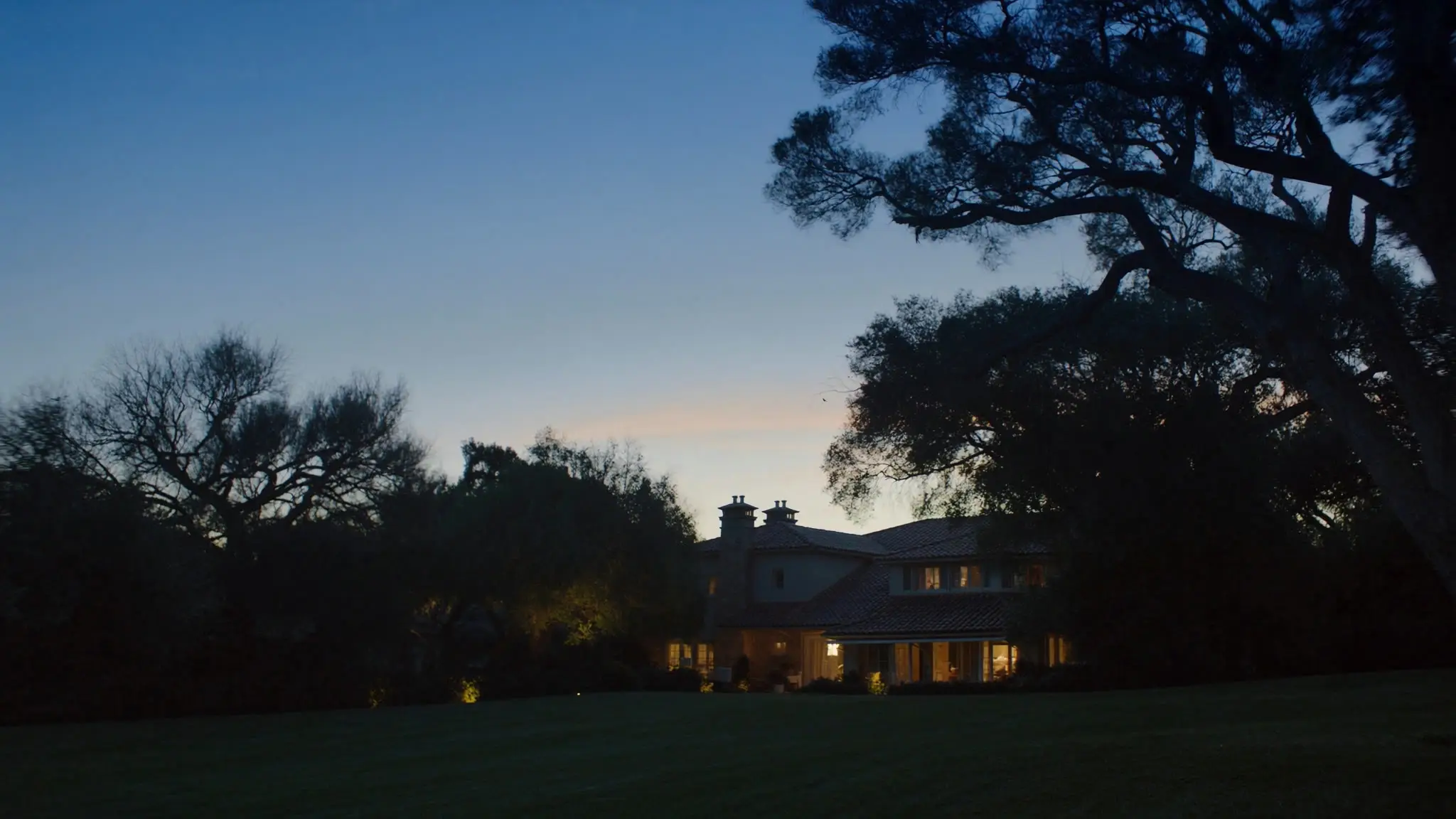 Tile-roofed La Cañada Flintridge home at dusk behind a broad oak-shaded lawn