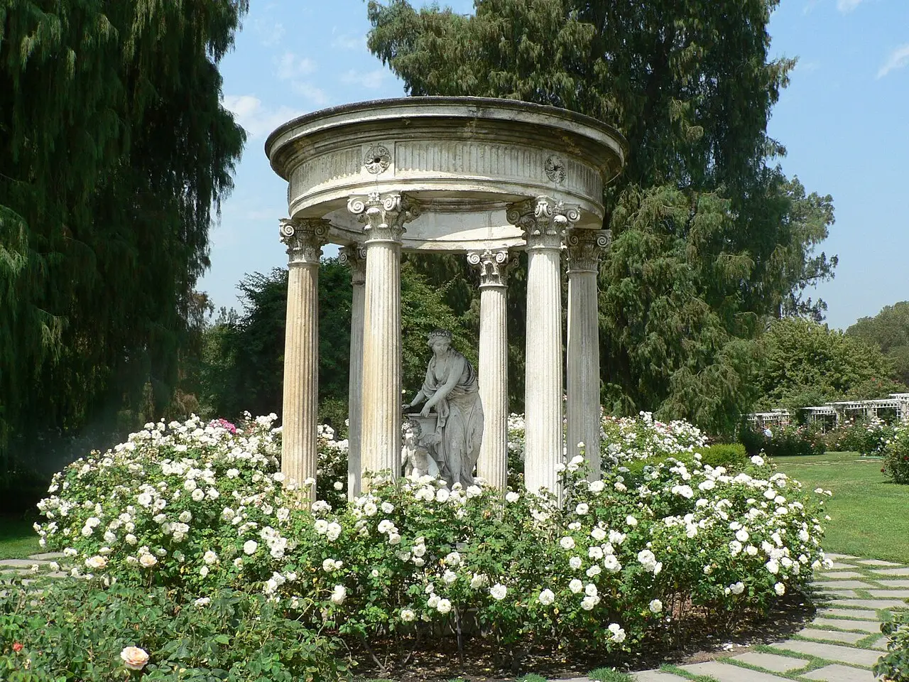 Classical stone gazebo ringed by white roses in a sunlit San Marino garden