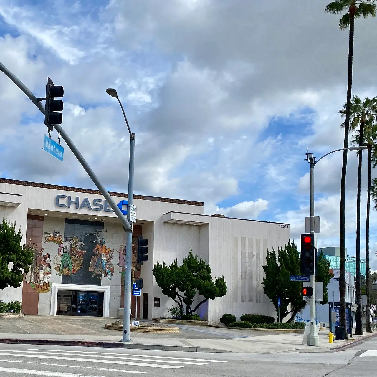 Corner bank building with a colorful mural under tall palms in Studio City