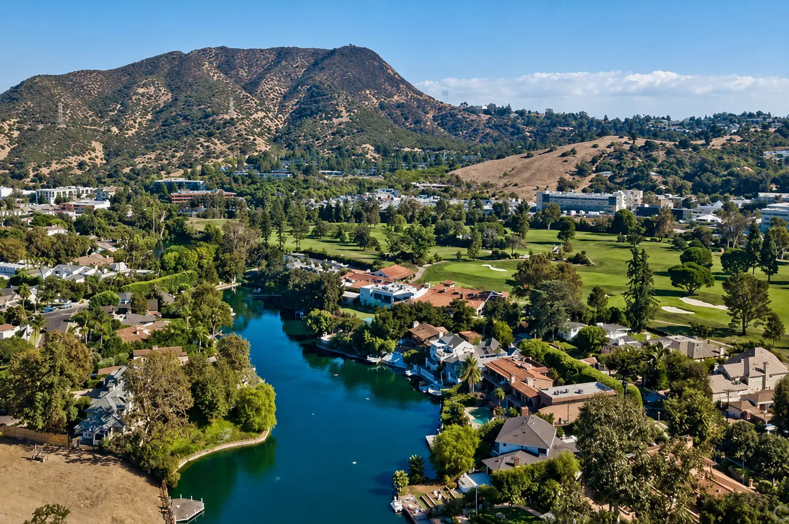 Aerial view of the private lake in Toluca Lake, ringed by homes with docks and a golf course, hills behind