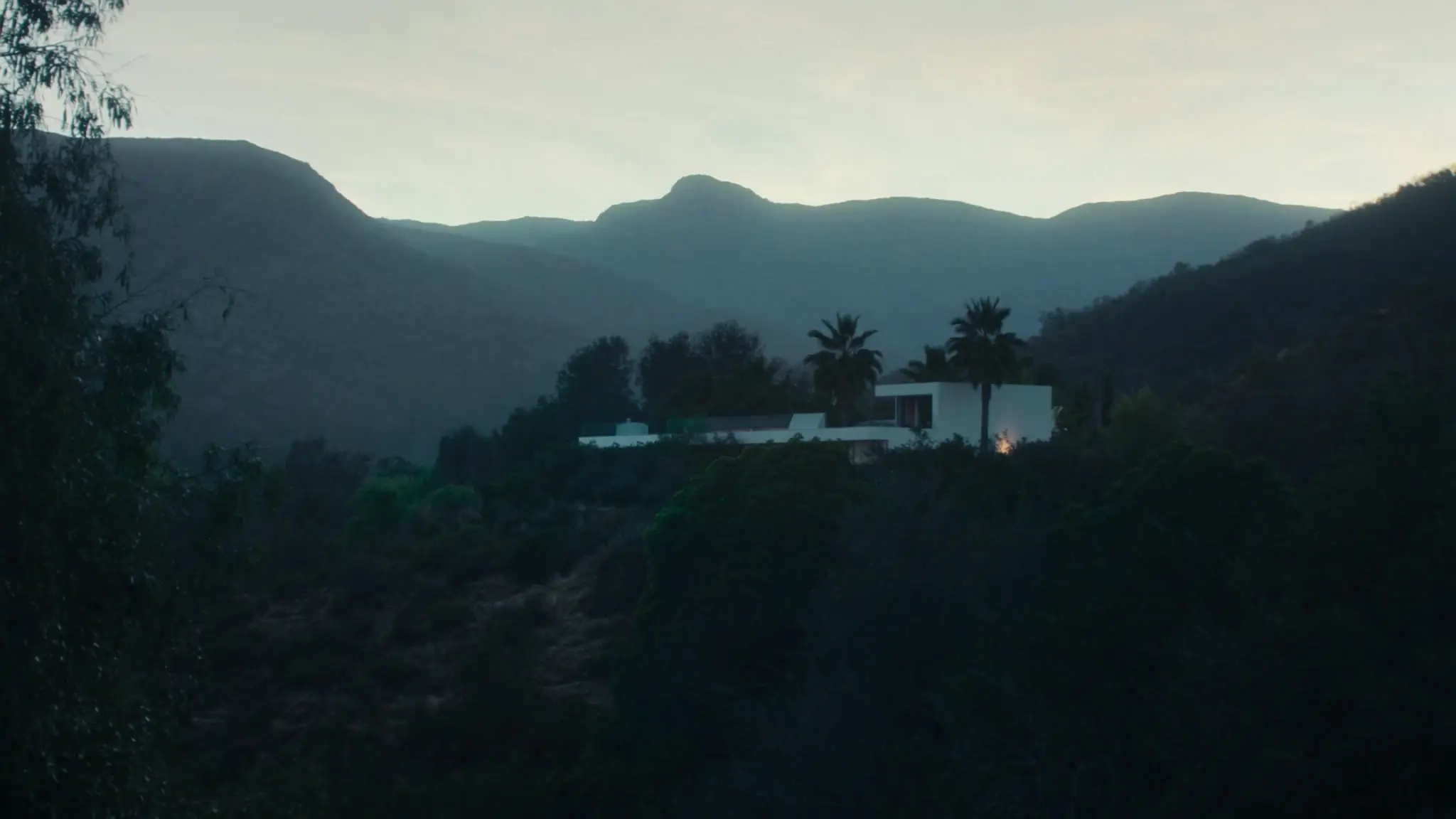 Modern white hillside house with palms above brushy Topanga canyon ridges at dusk