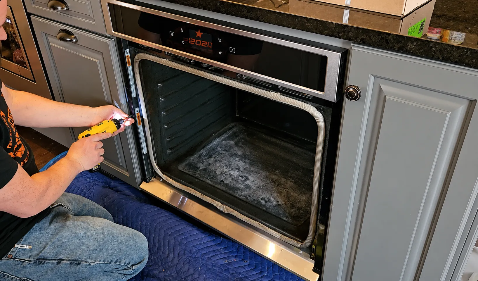 A technician repairing a wall oven pulled onto a padded work blanket